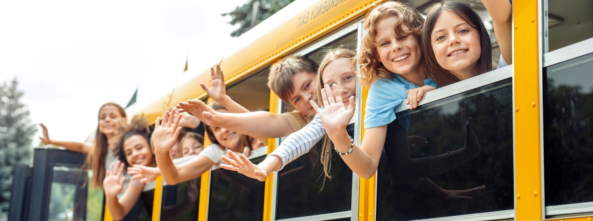 children waving from the window of a school bus