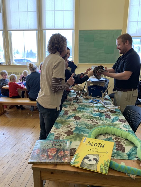 families meeting a ball python with the zoo keeper in a classroom